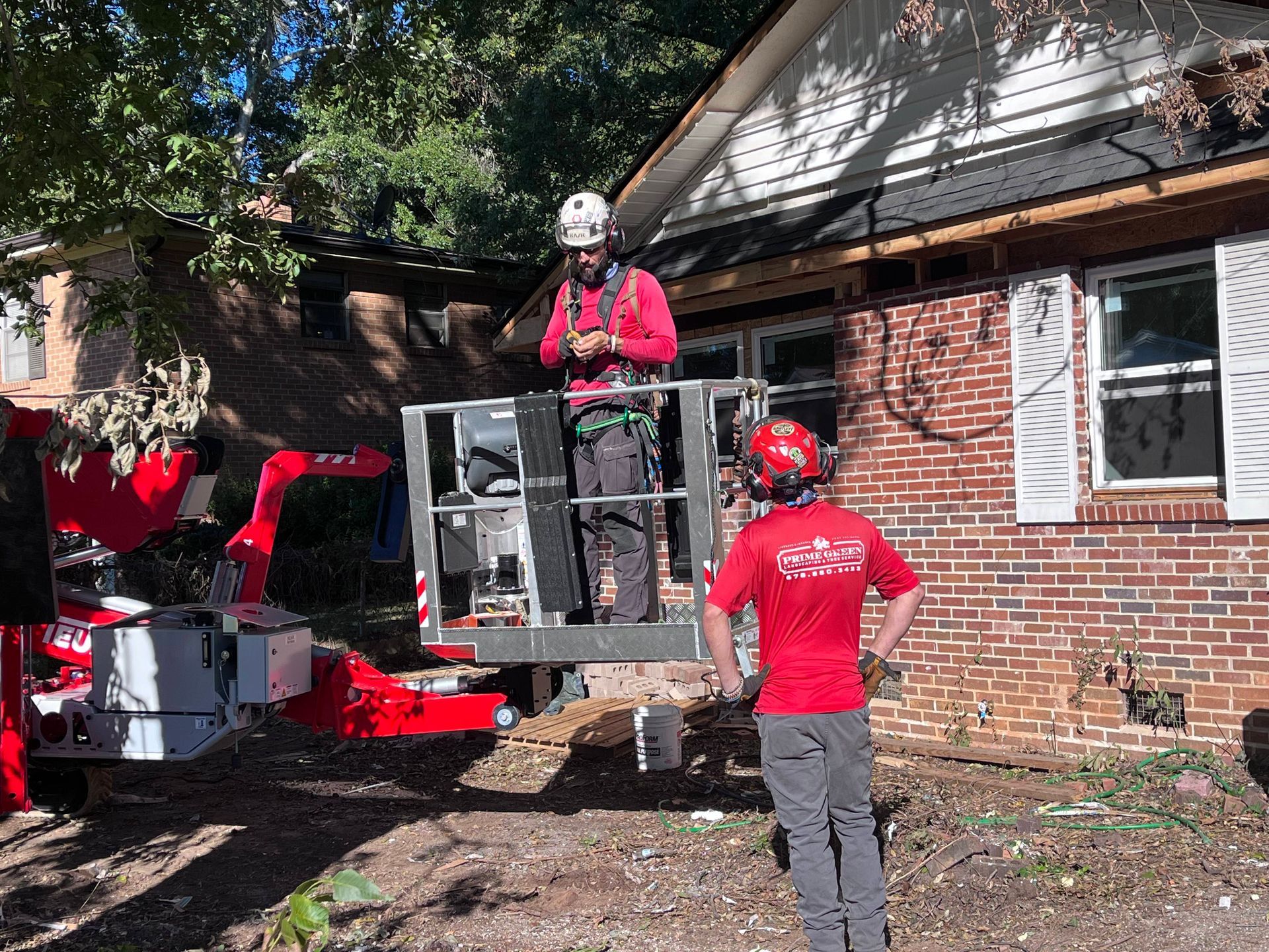A man in a red shirt is standing in front of a brick house.
