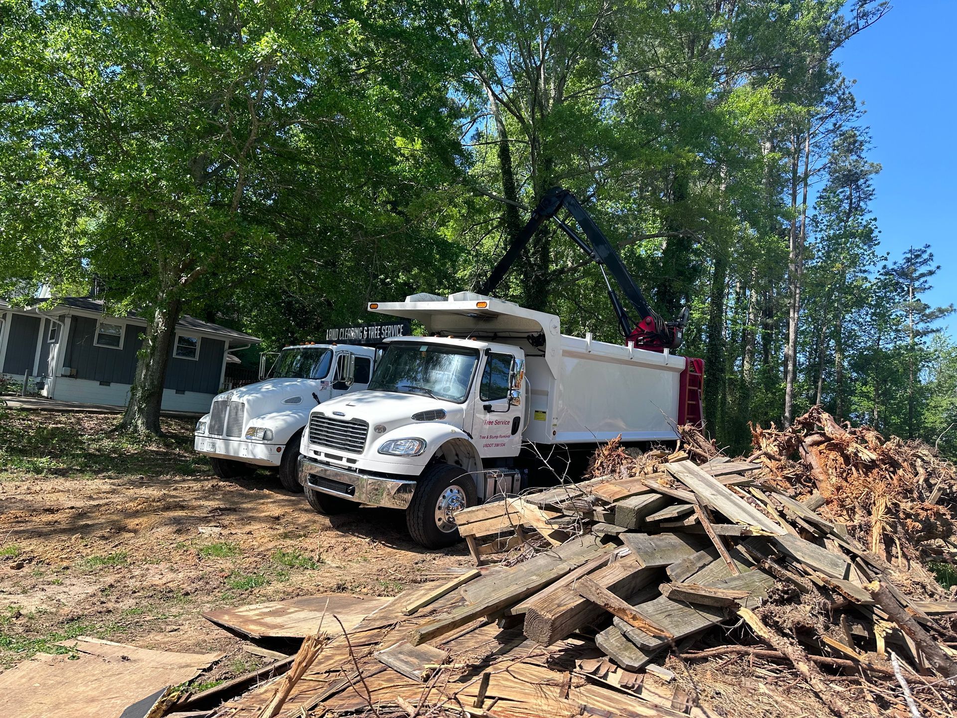 Two dump trucks are parked next to a pile of wood.