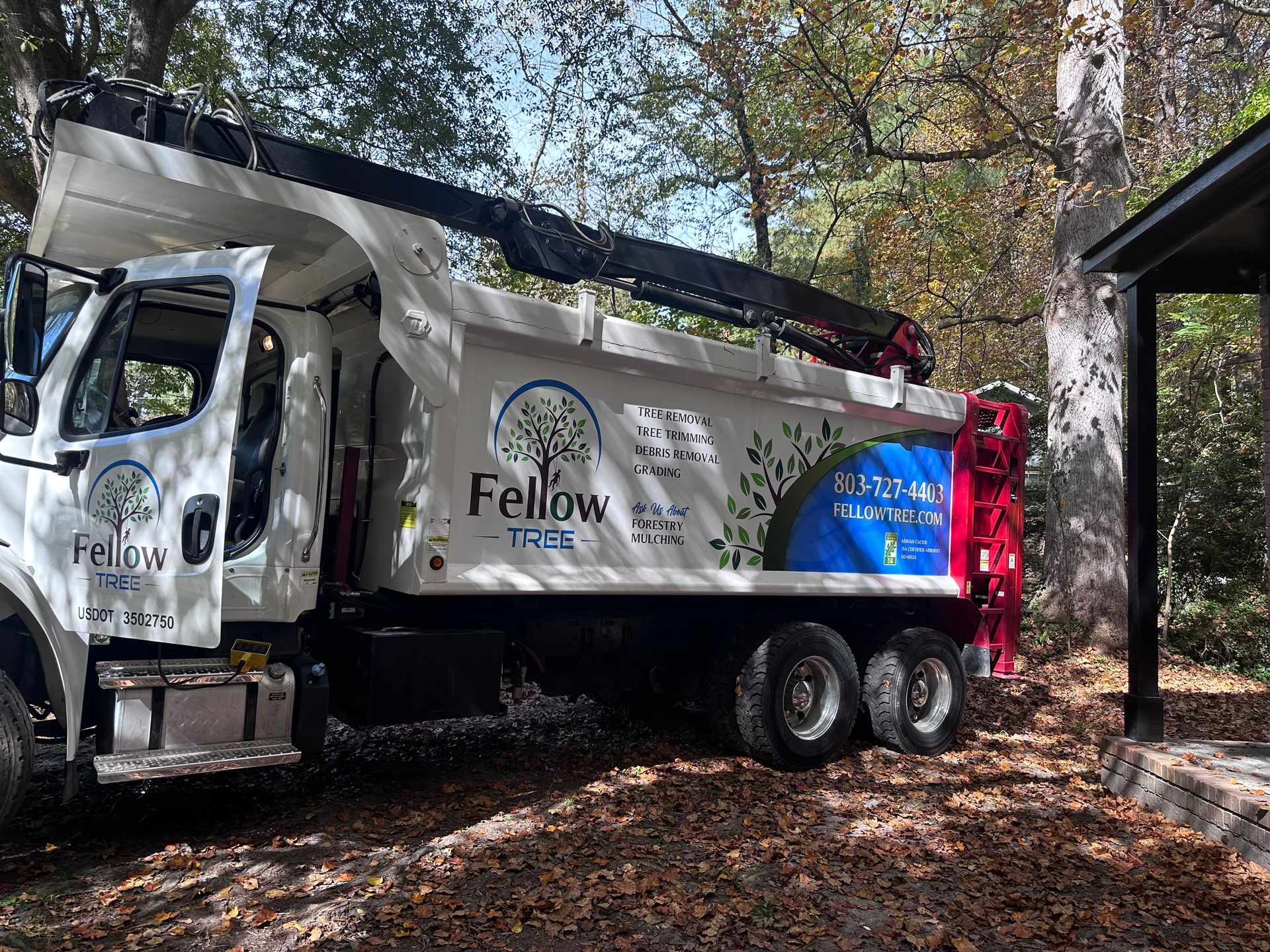 A dump truck with a crane attached to it is parked in the woods.
