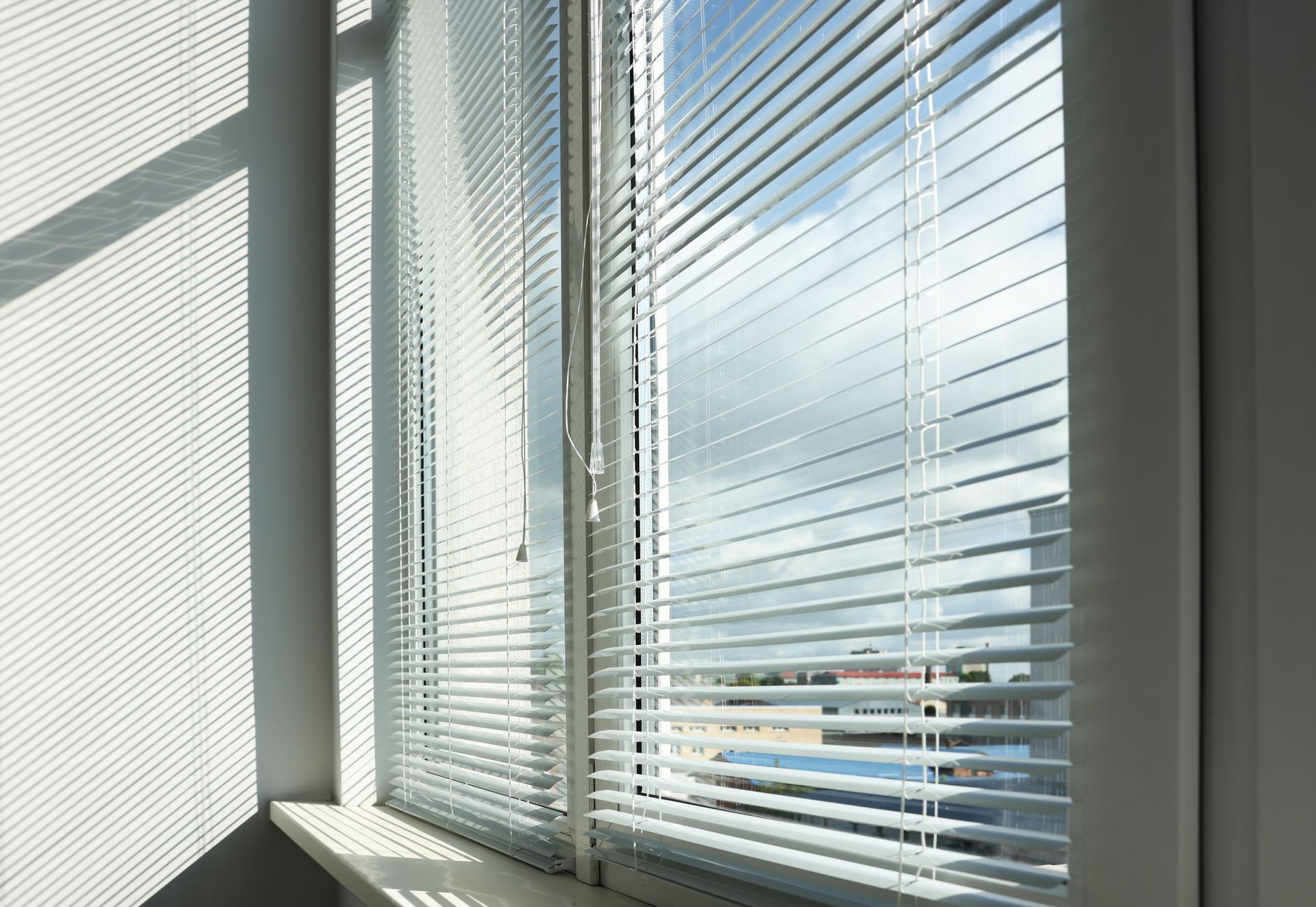 Sunlit office window with white blinds casting shadows on a wall and windowsill Sunlit office window with white blinds casting shadows on a wall and windowsill