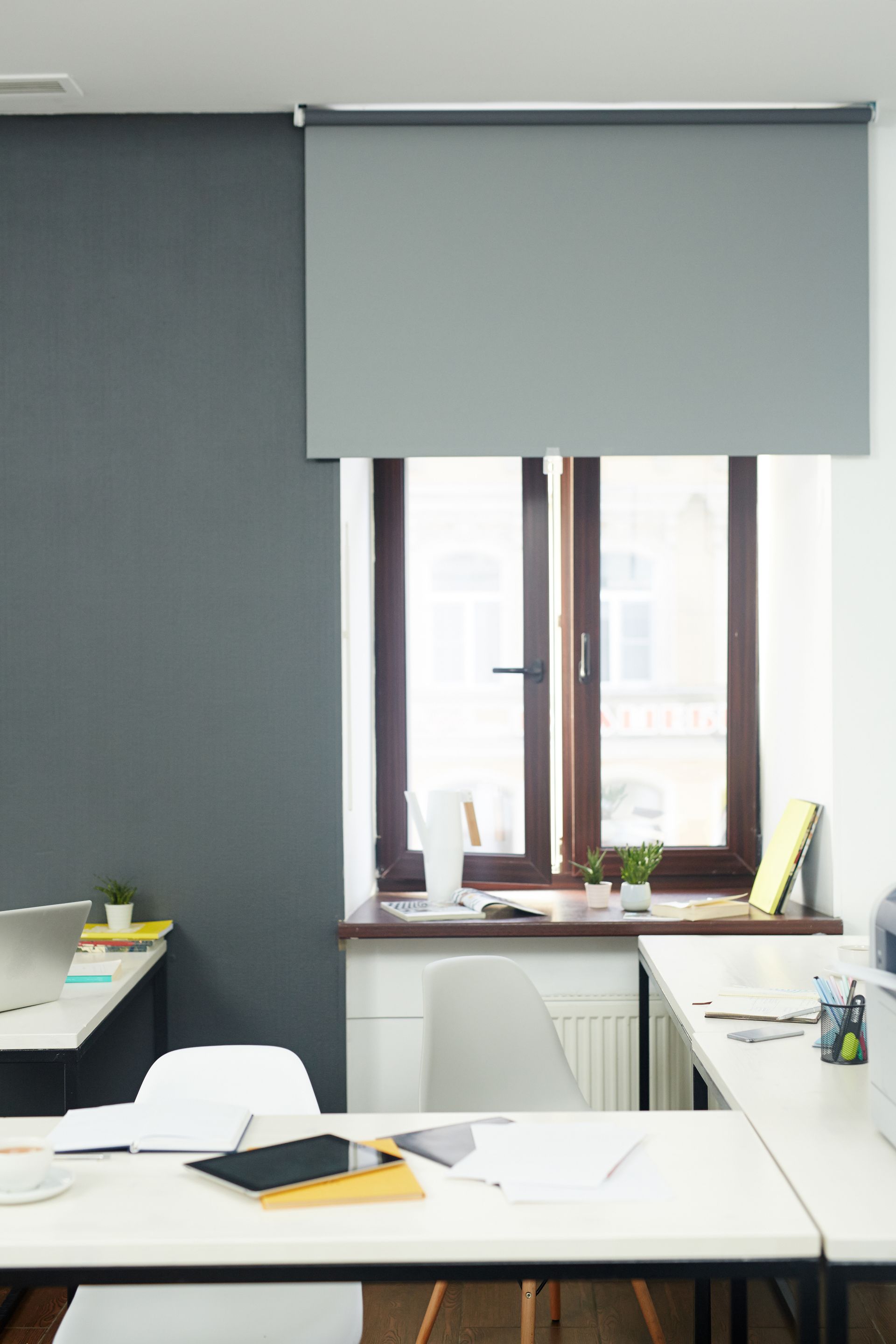 Quiet office with a large window, white desk, and gray roller blind. Quiet office with a large window, white desk, and gray roller blind.