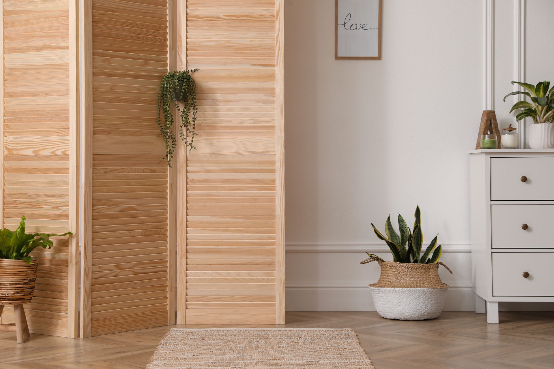 Bright minimalist room with wooden folding screen, potted plants, rug, and white drawers