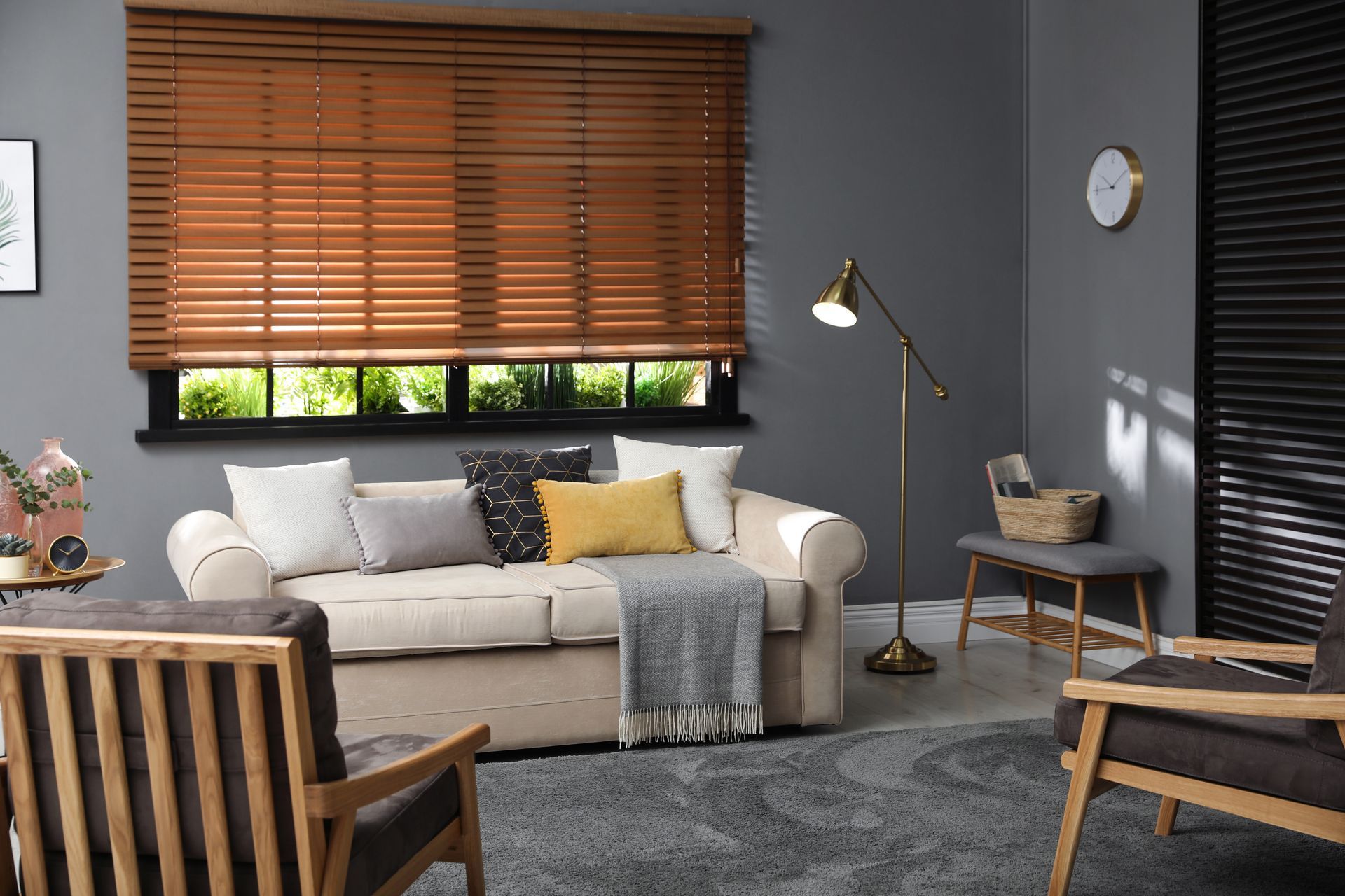 Cozy living room with beige sofa, wood blinds, gray rug, floor lamp, and wicker chair accents Cozy living room with beige sofa, wood blinds, gray rug, floor lamp, and wicker chair accents
