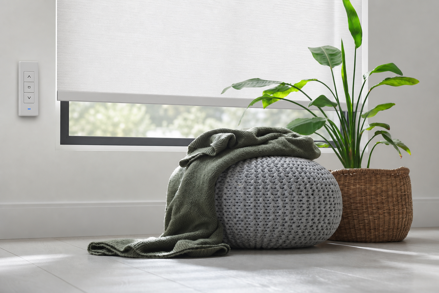 Cozy gray ottoman with green throw beside a wicker basket plant under a window shade