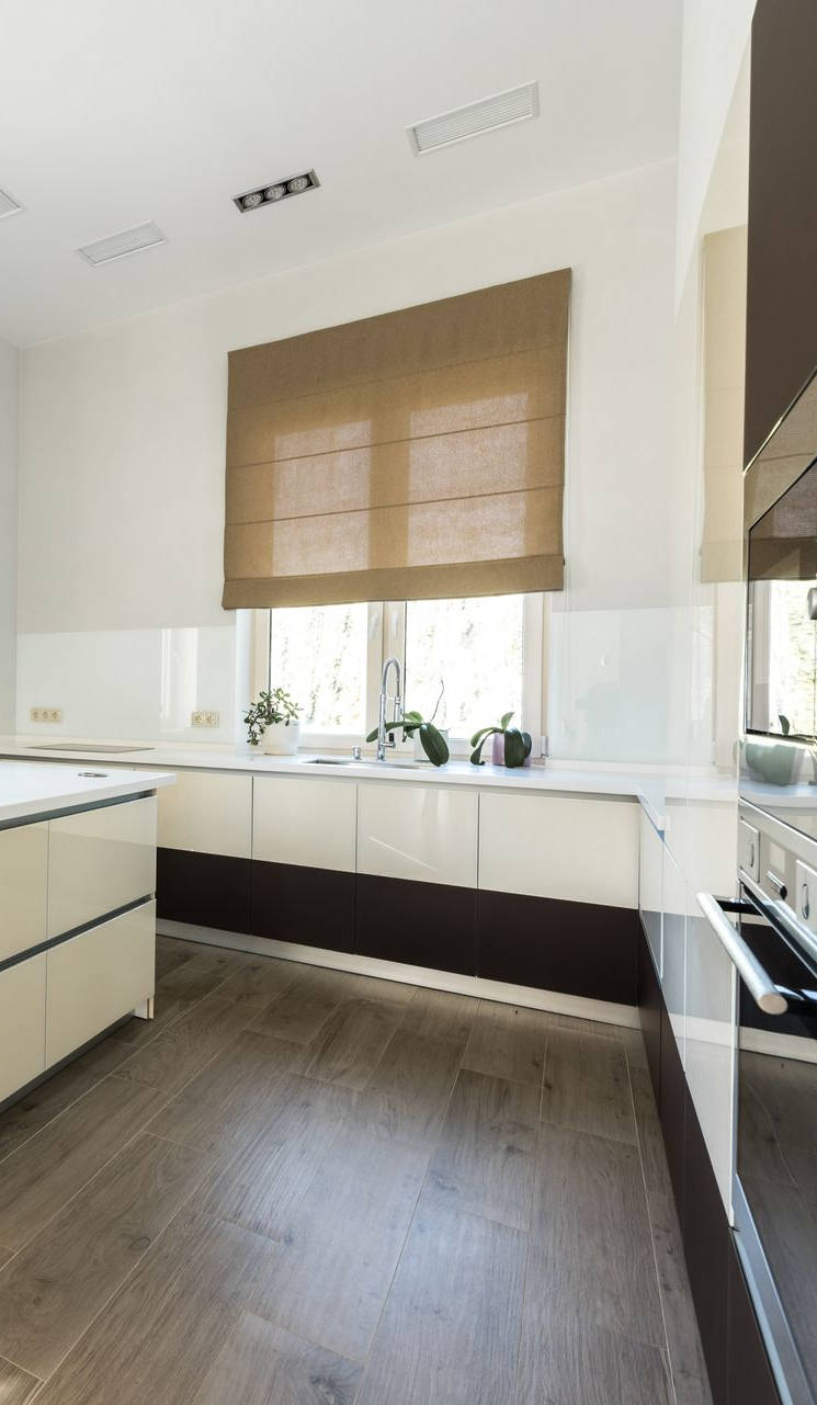 Modern kitchen with dark cabinets, wood floor, white countertops, and a window with woven blinds.
