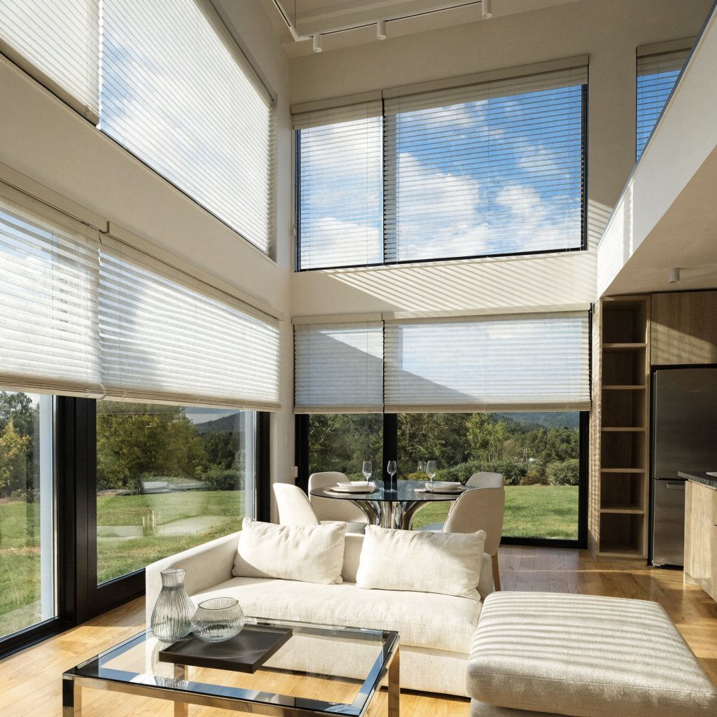 Bright modern living room with tall windows, white sofa, glass table, and lounge chair overlooking greenery Bright modern living room with tall windows, white sofa, glass table, and lounge chair overlooking greenery
