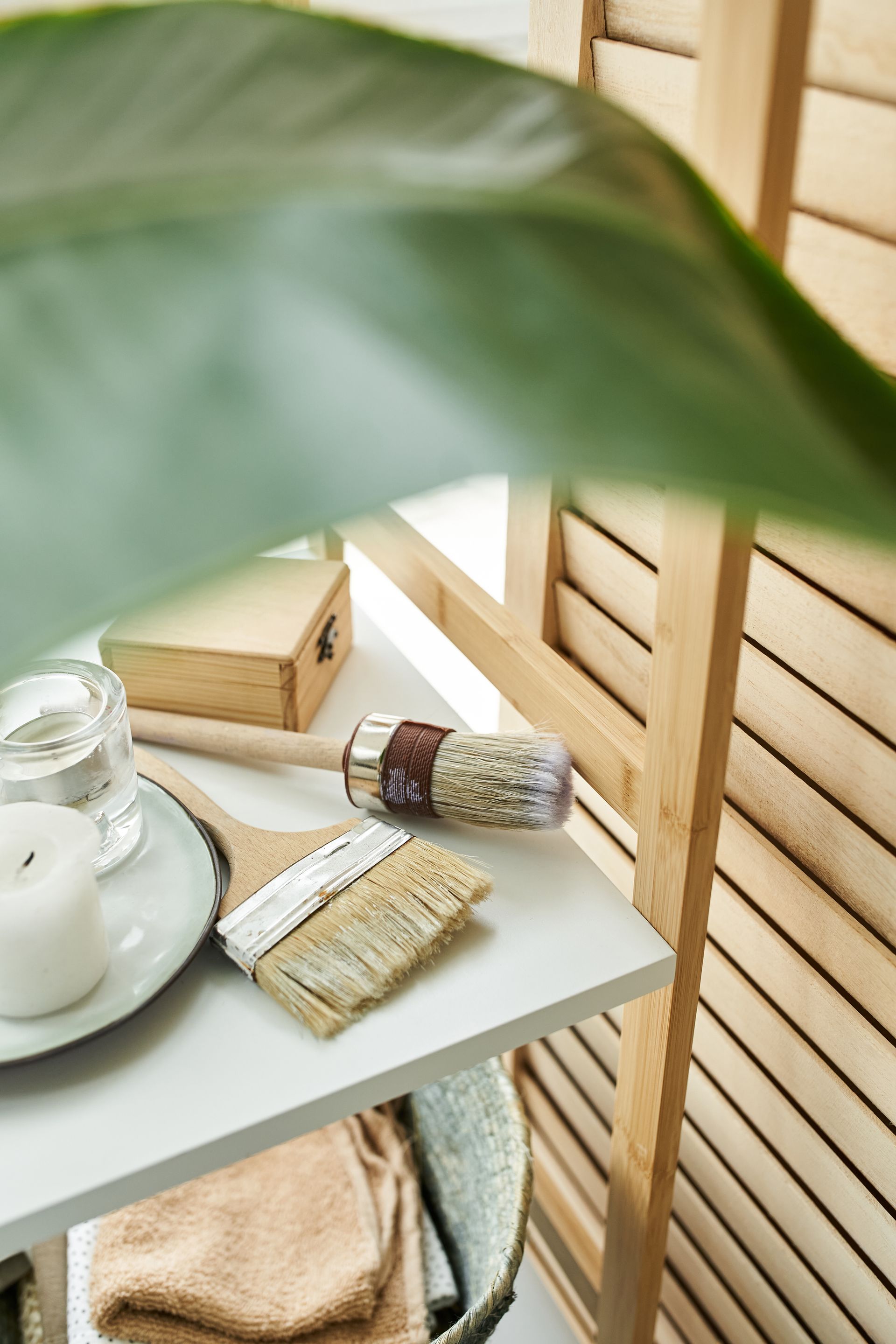 Sage green spa tray with candle, rolled towels, and bath accessories beside a wooden slatted wall