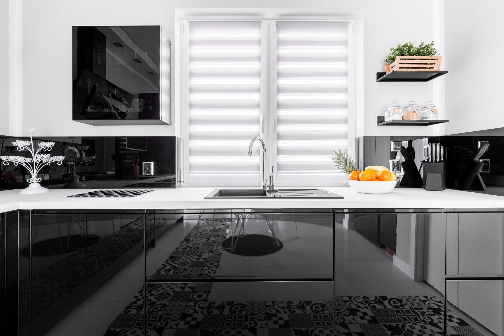 Modern black-and-white kitchen with glossy cabinets, window above sink, and shelves with plants and fruit