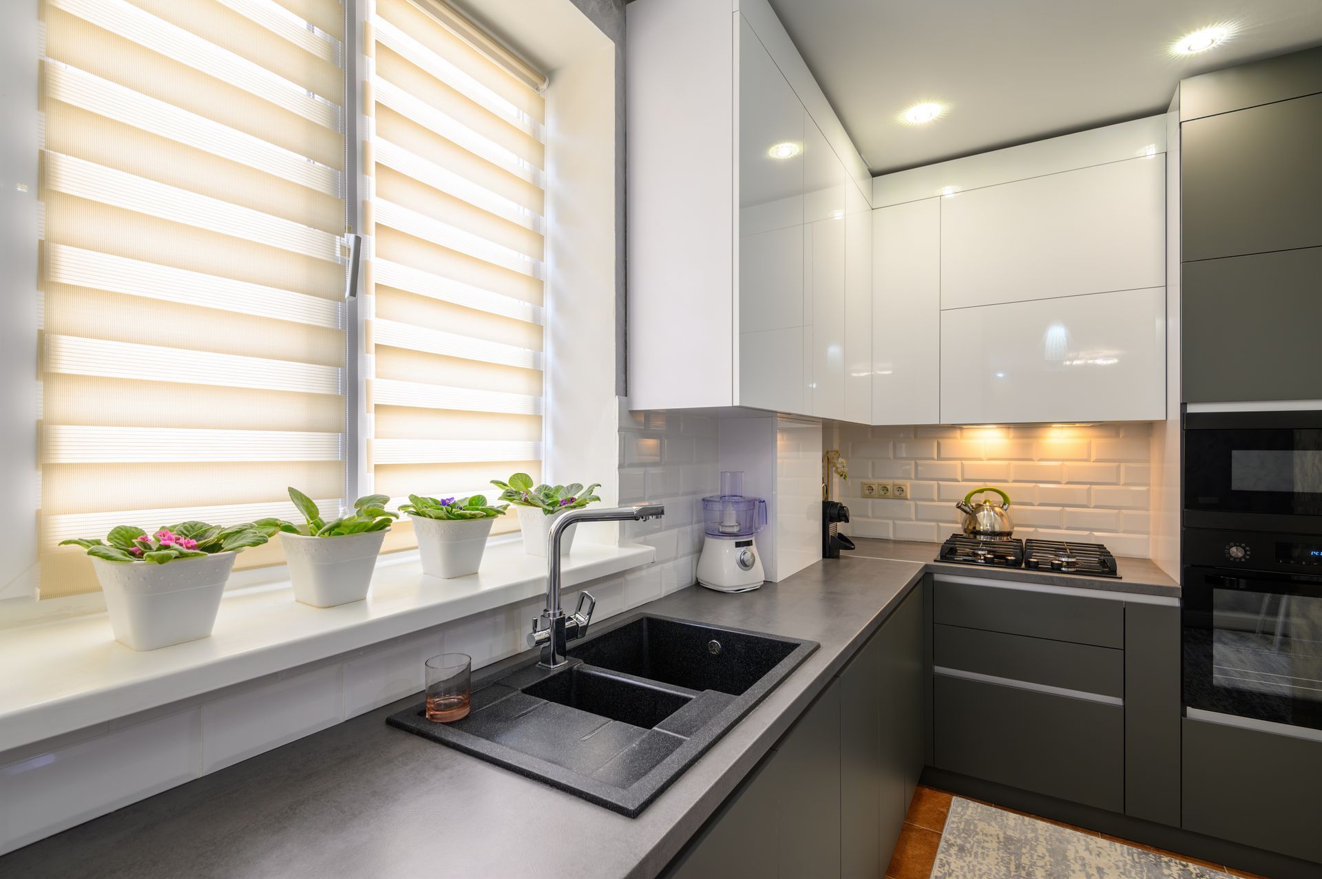 Modern kitchen with black sink, white cabinets, and window with potted plants