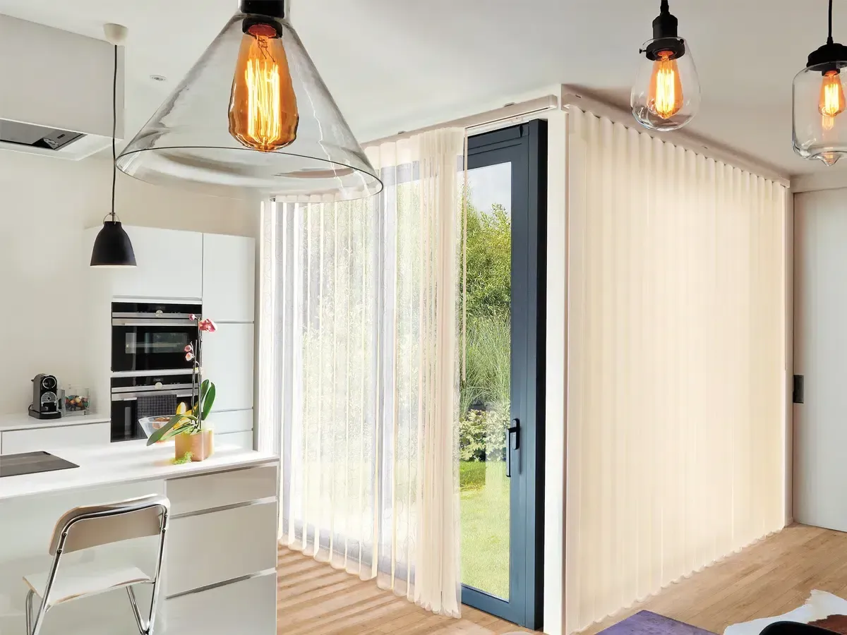 Bright modern kitchen and dining area with sliding glass doors and sheer curtains opening to a green backyard.