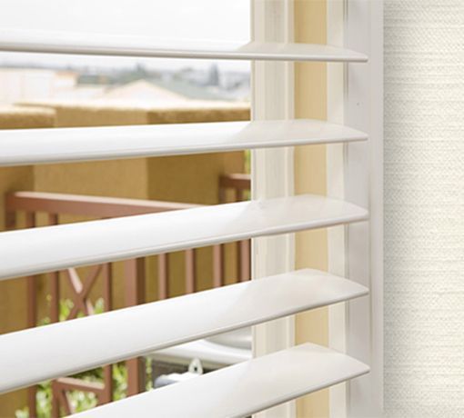 White window blinds partly open, showing a bright outdoor view through a window.