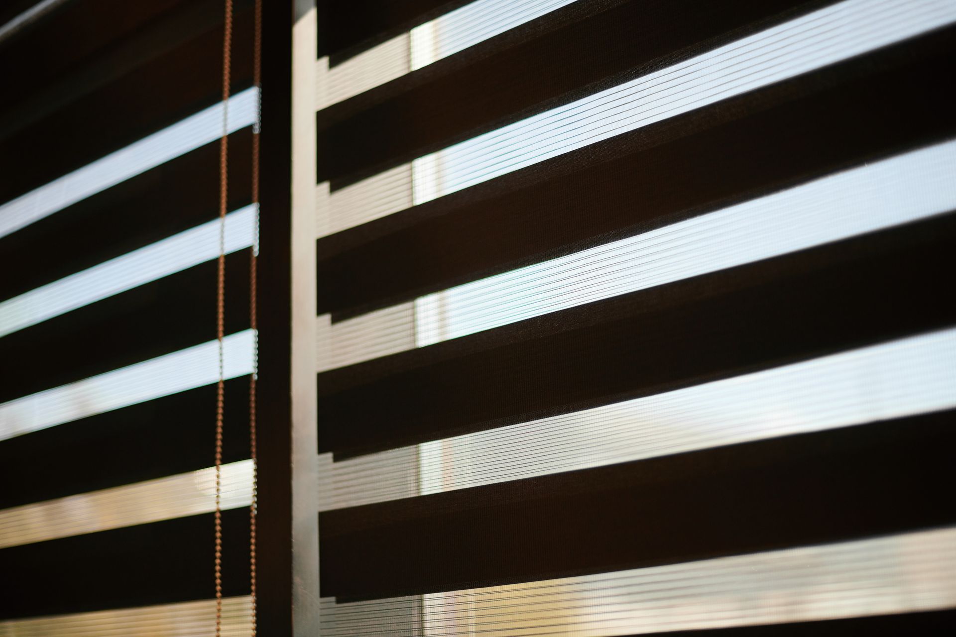 Sunlight filtering through partially closed horizontal blinds, casting striped shadows