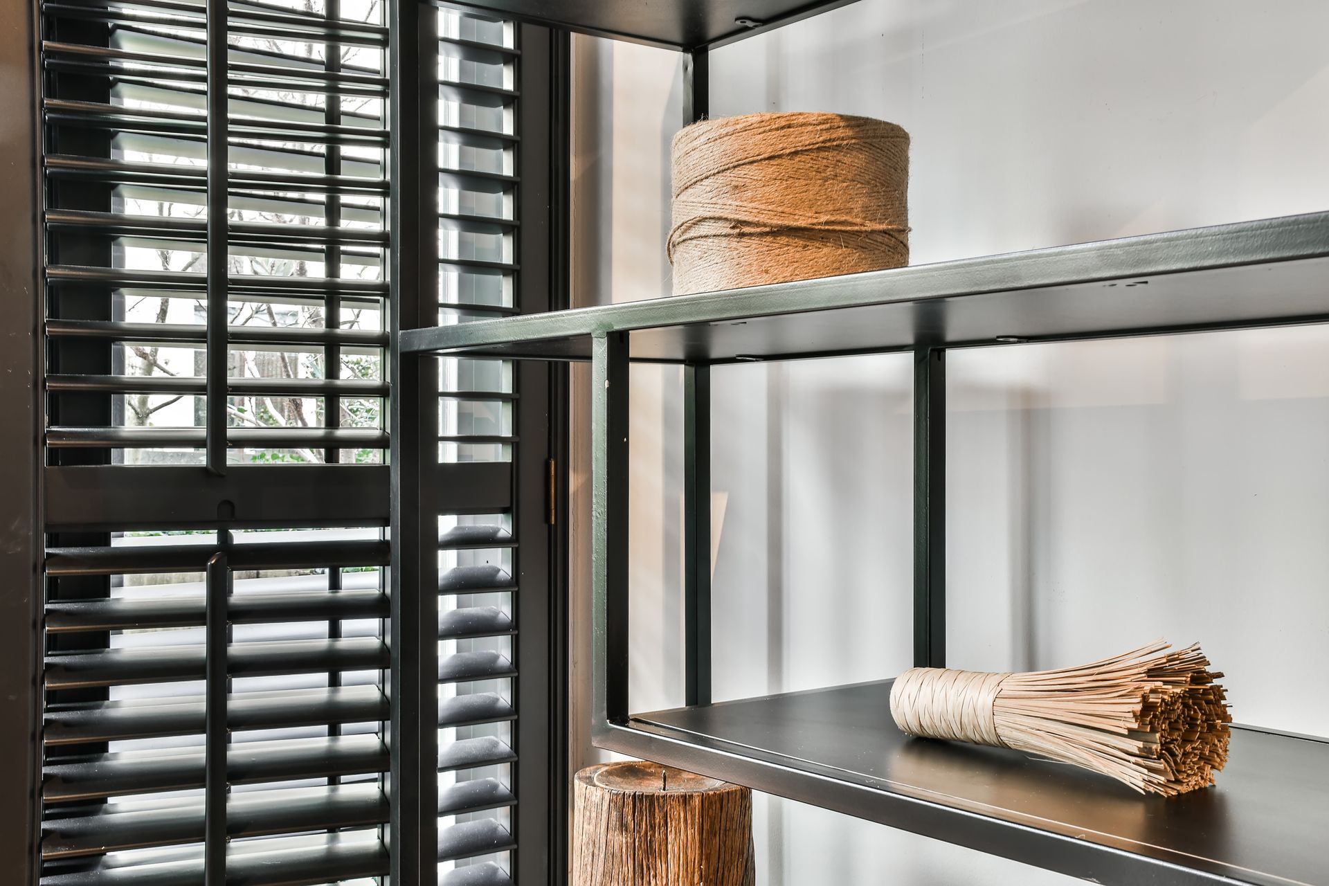 Metal shelving by a window with woven baskets and a broom in a bright room