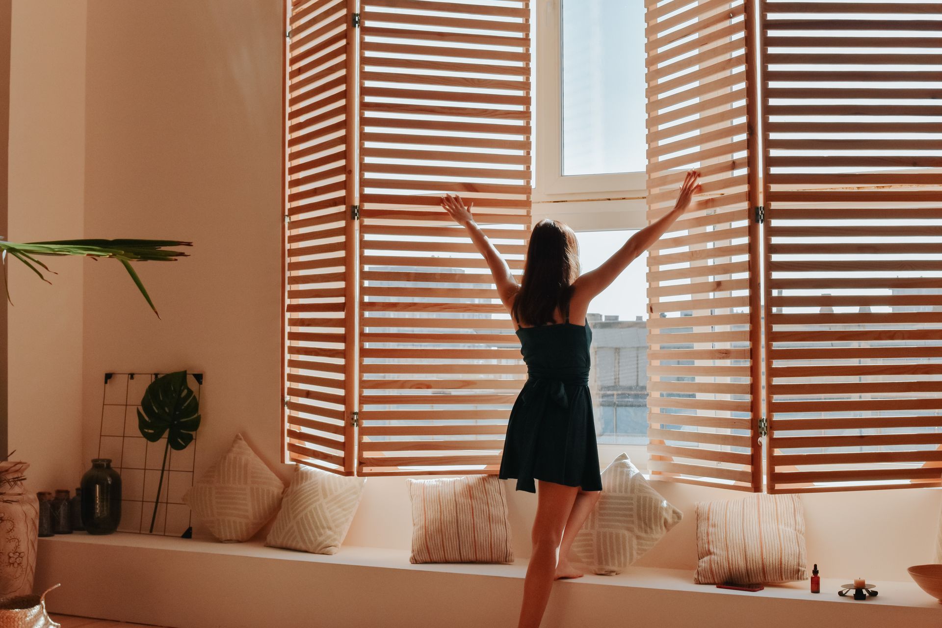 Person stretching by a sunlit window with wooden blinds in a cozy living room