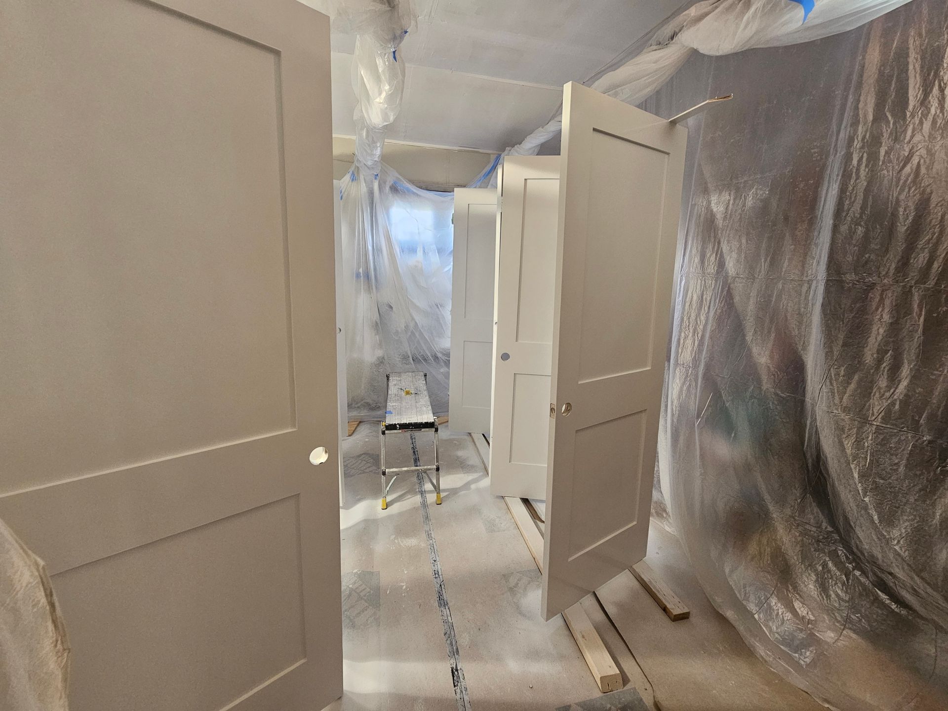 Person in yellow hard hat paints a white wall gray with a roller on a long handle, exterior setting.