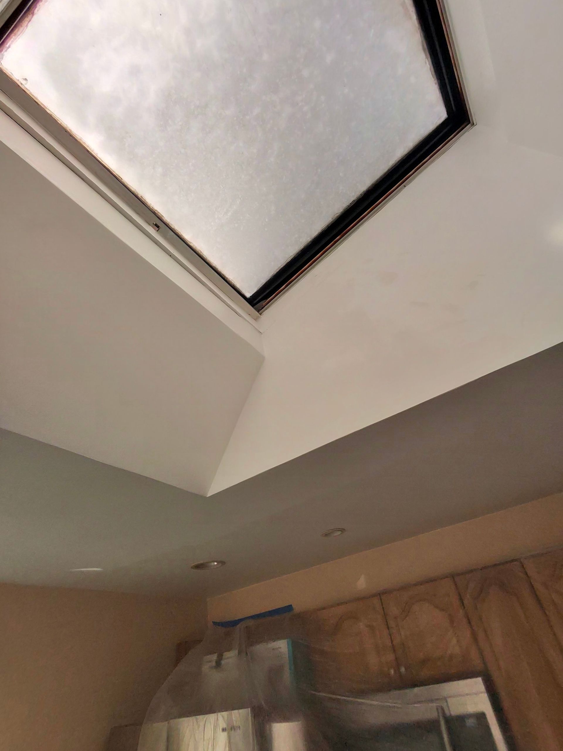 Person painting a wall in a room; ladder, paint bucket, dark grey and white walls, black and white ceiling, and doors.