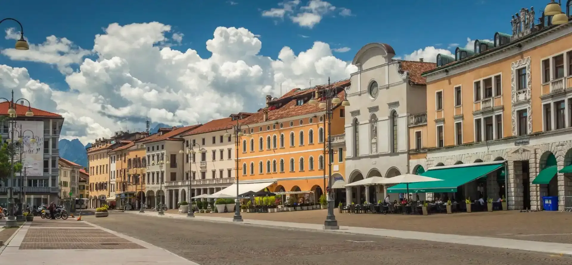 Gli edifici fiancheggiano una piazza acciottolata, il cielo è azzurro e le nuvole sono soffici.