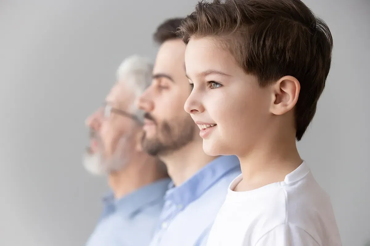 Tre generazioni di una famiglia: nonno, padre e figlio, tutti rivolti nella stessa direzione con un leggero sorriso.