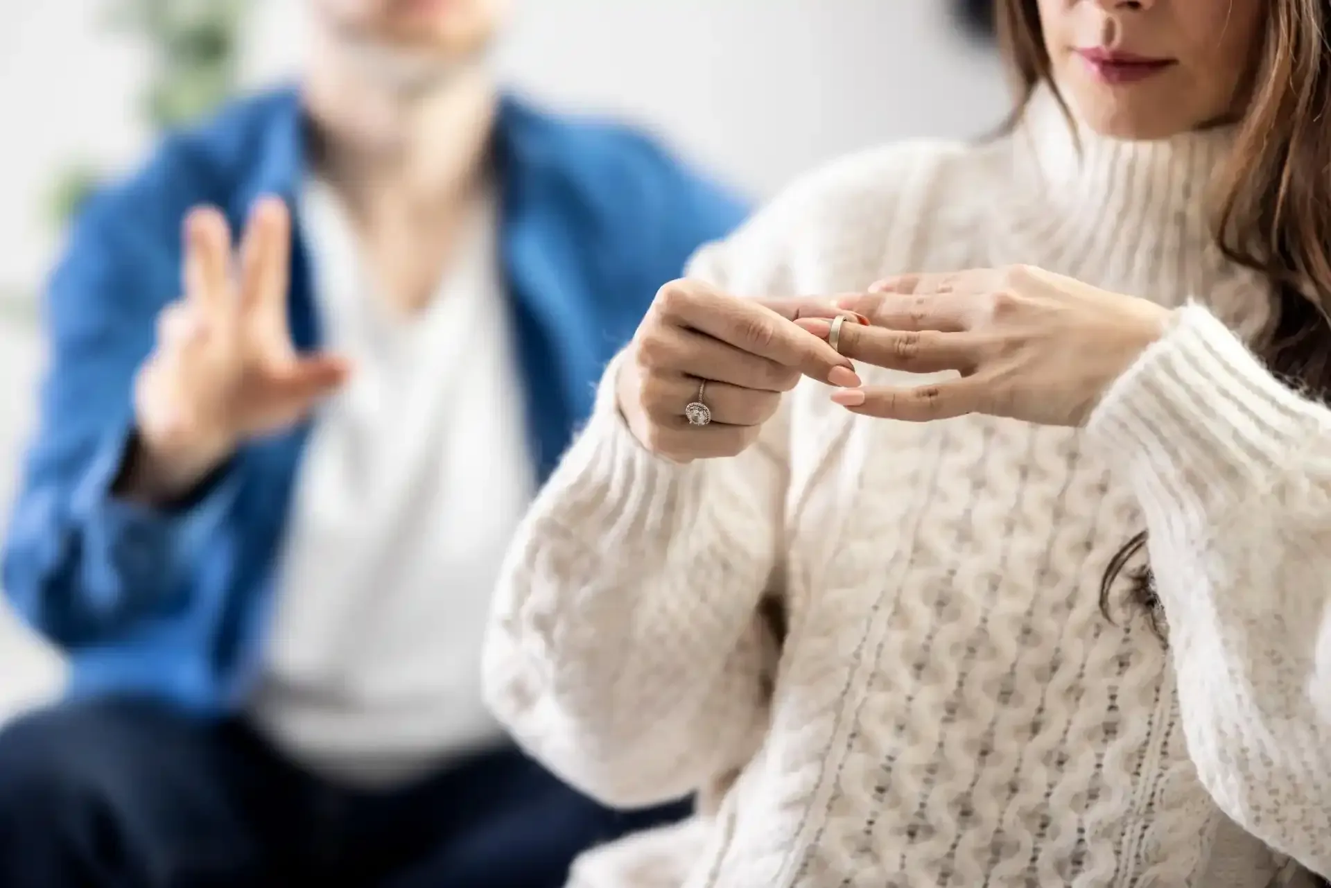 Una donna si toglie un anello mentre un uomo gesticola sullo sfondo, suggerendo una conversazione difficile.