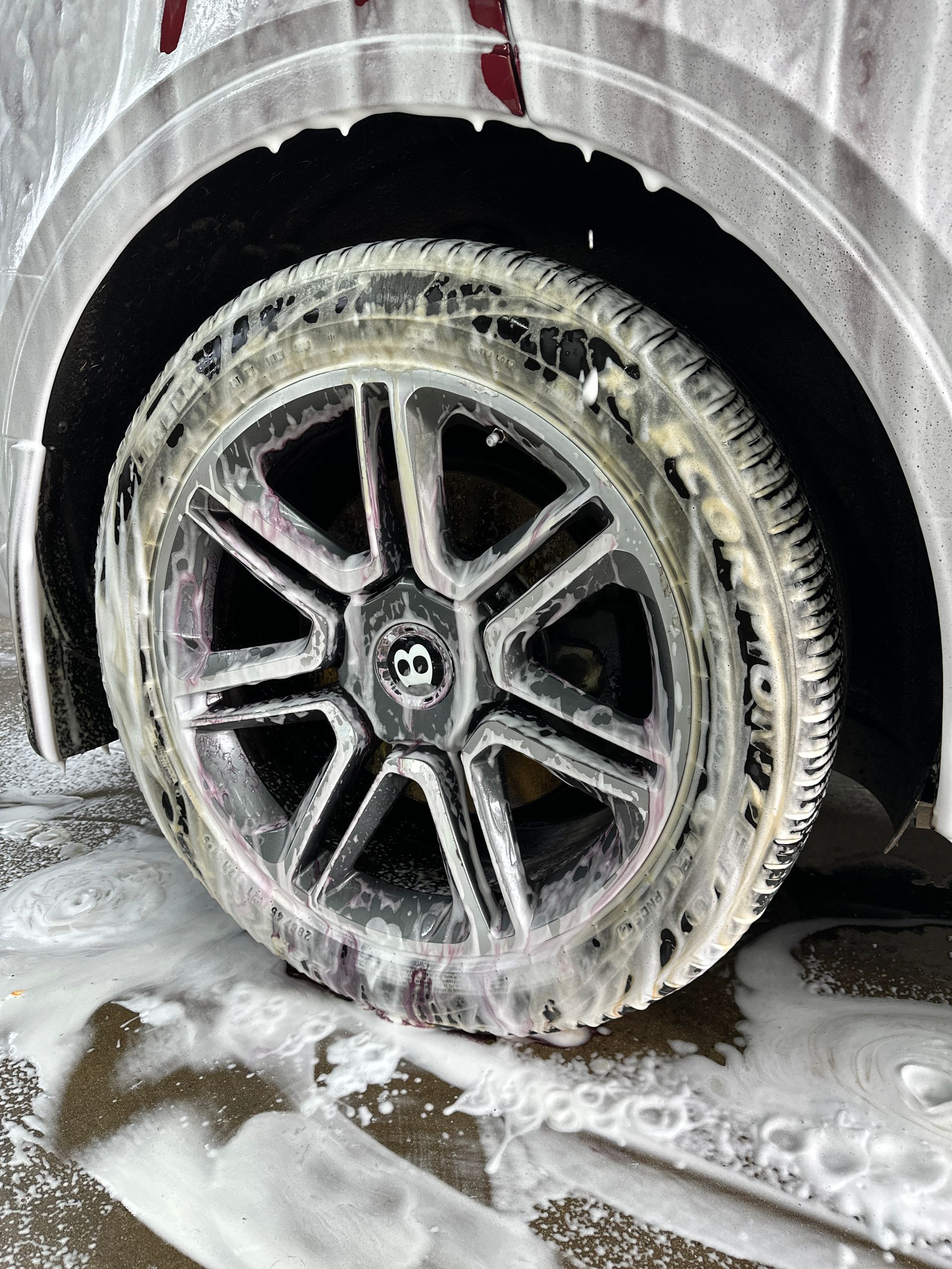 A Bentley car wheel covered in white soap suds during a car wash.