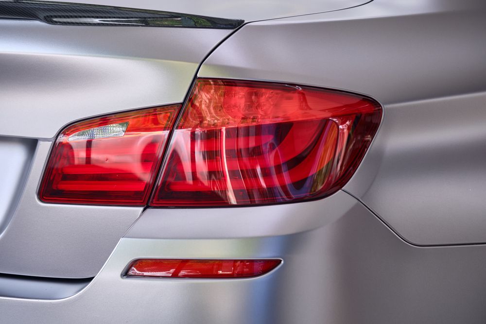 Close-up of a silver car's matte-finish body, rear taillight, and bumper reflector.
