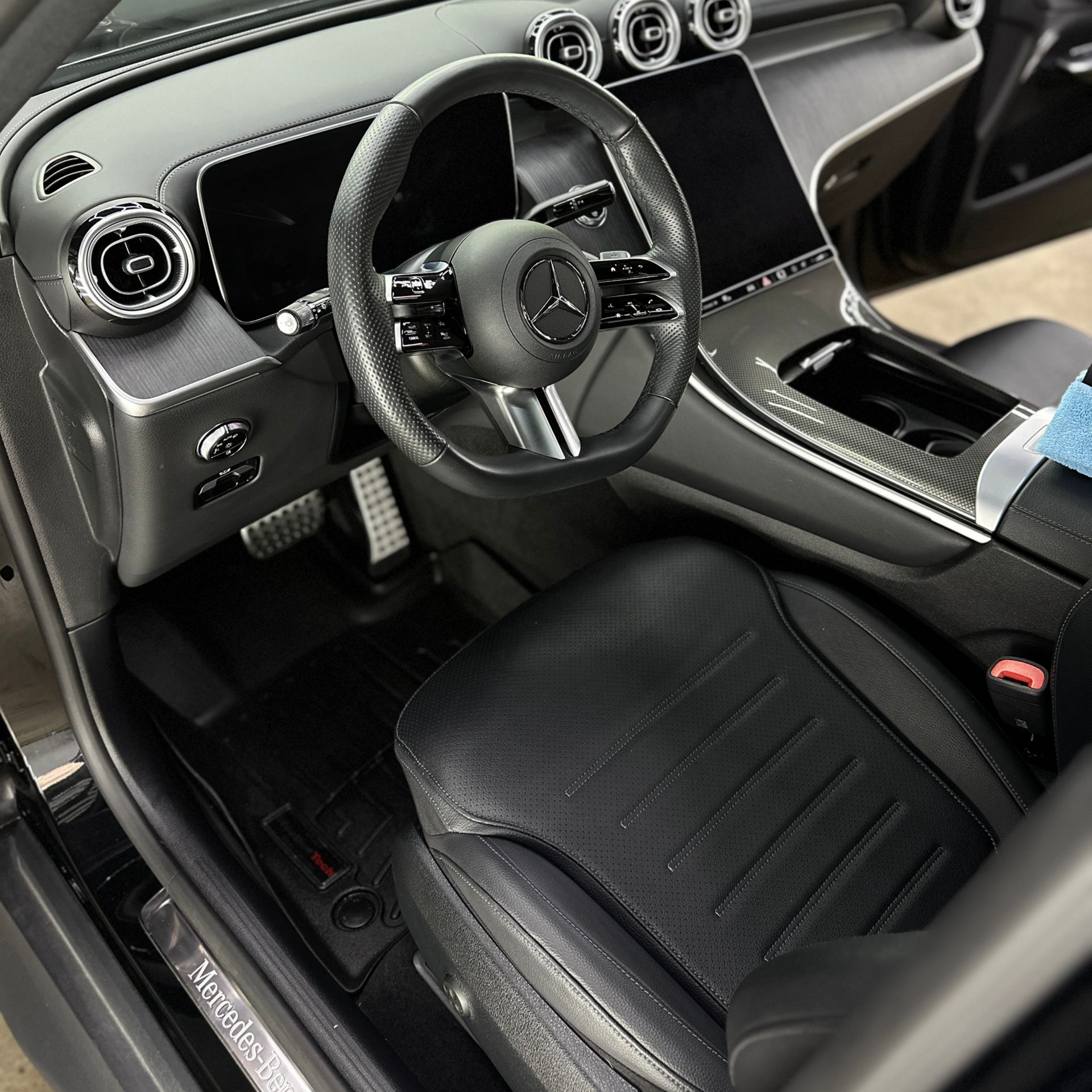 Interior of a modern Mercedes-Benz with a leather-wrapped steering wheel, digital dashboard, and black leather seating.