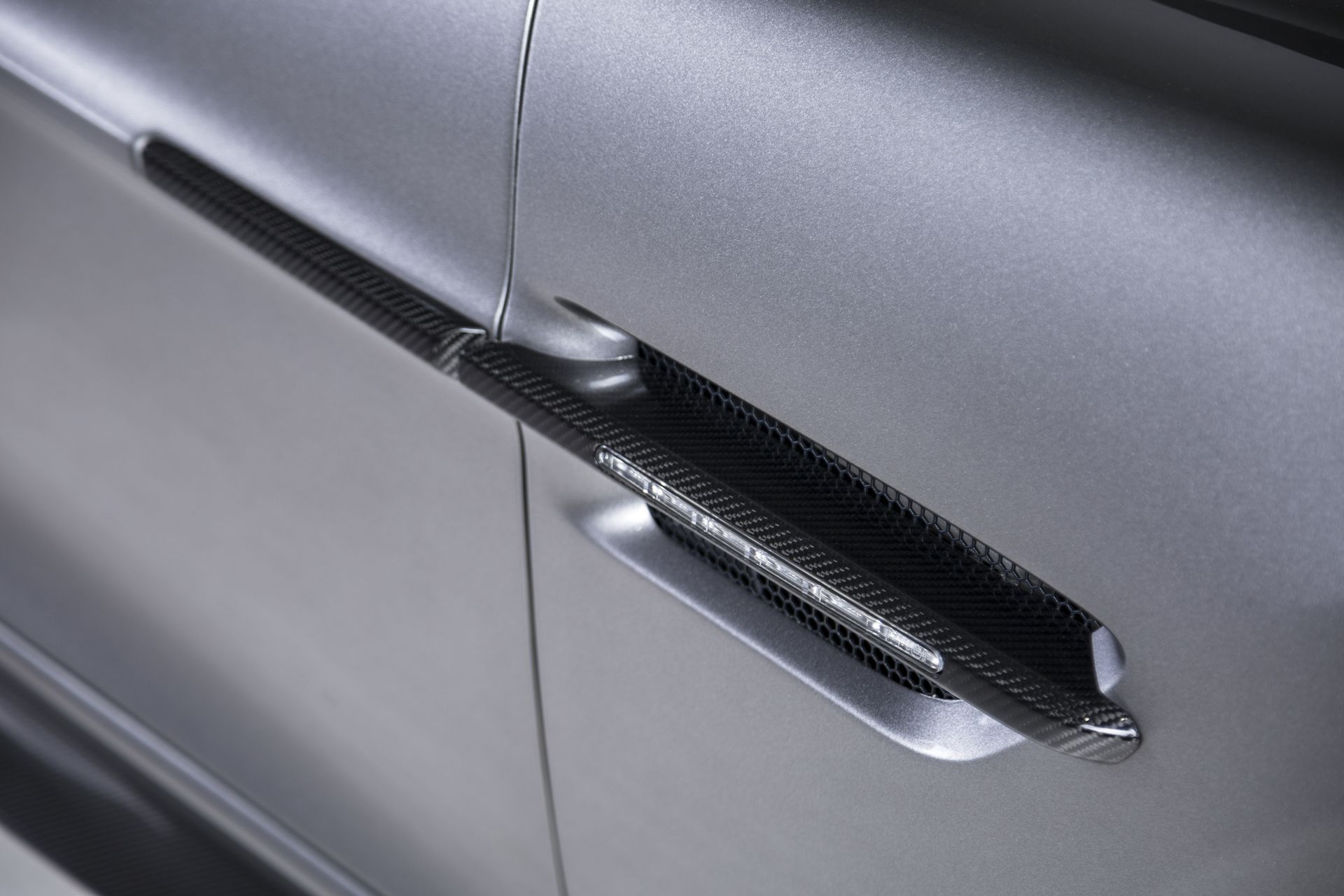 Close-up of a carbon fiber side vent on a matte silver car door.