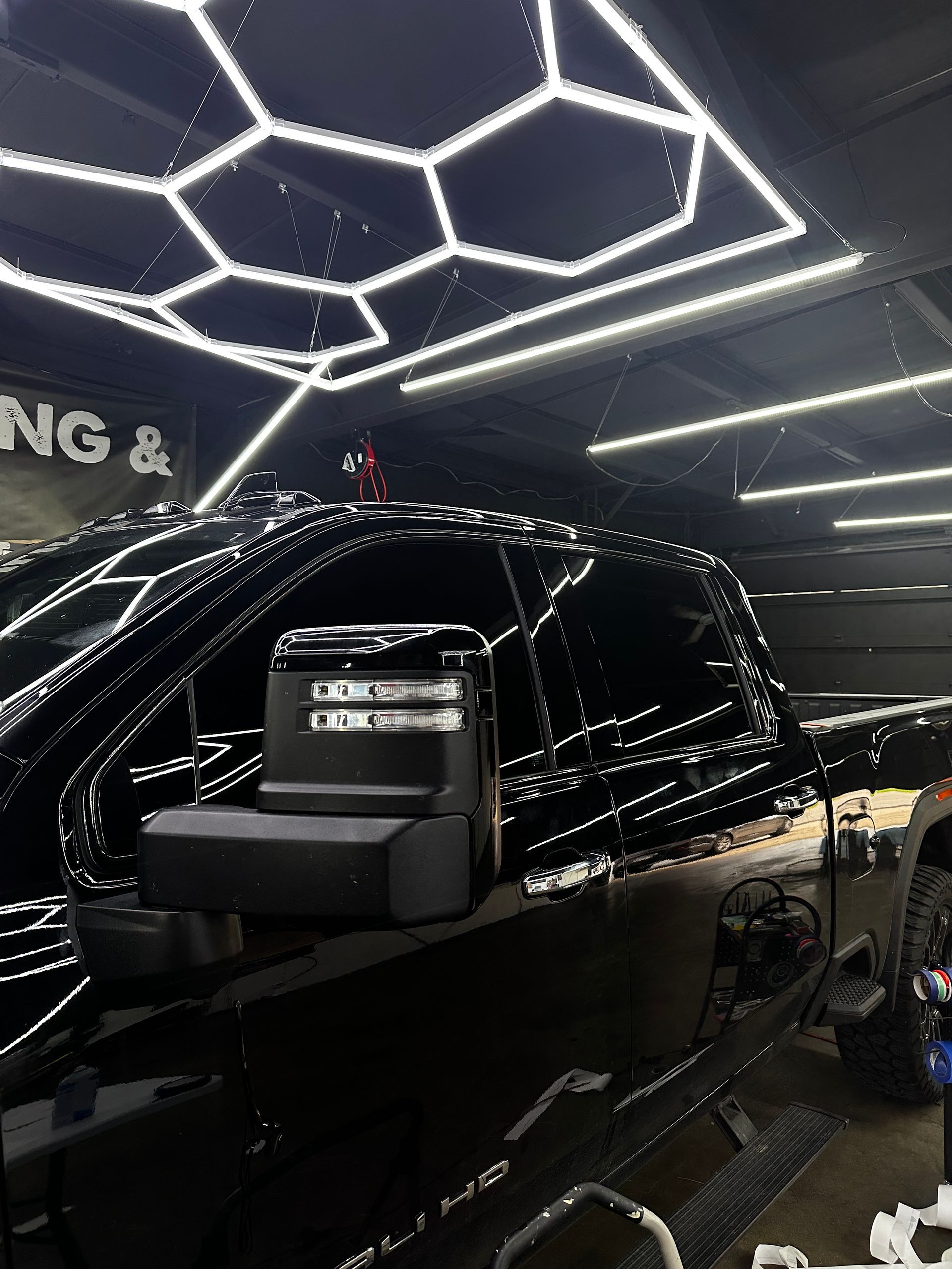 A black truck parked in an indoor garage under bright, hexagonal LED ceiling lights.
