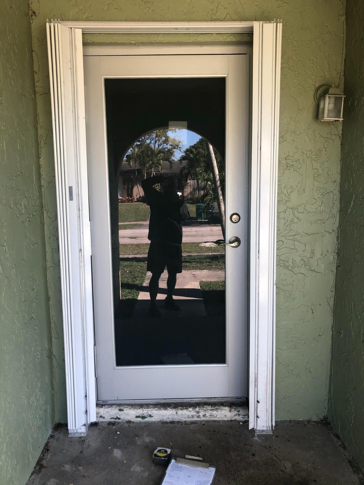 A man is standing in front of a door with a reflection of him in the glass.