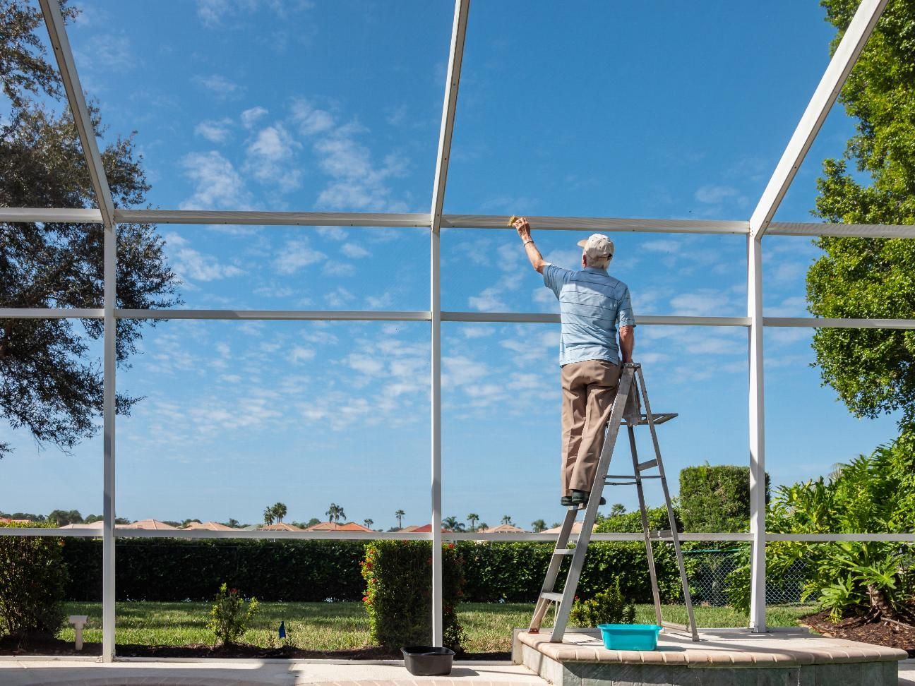 A man is standing on a ladder cleaning a pool screen.