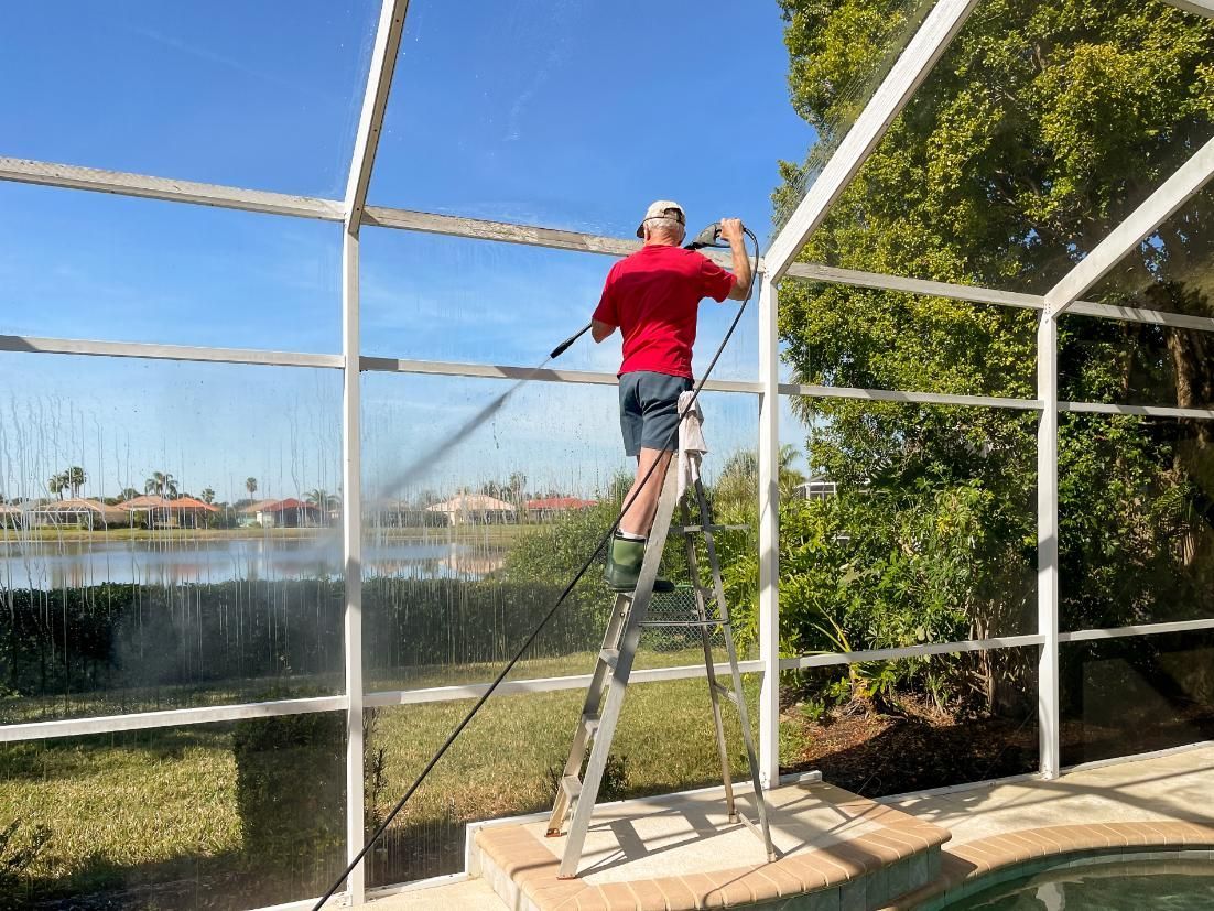 A man is standing on a ladder cleaning a pool screen.