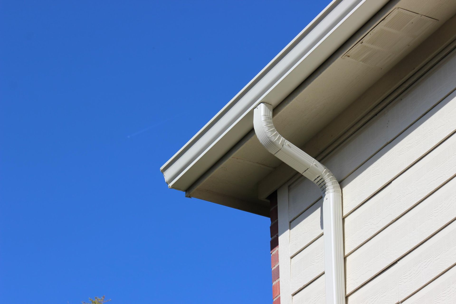A gutter on the side of a house with a blue sky in the background.