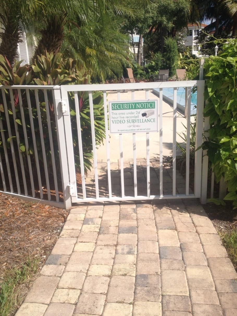 A white gate leading to a pool with a sign on it.