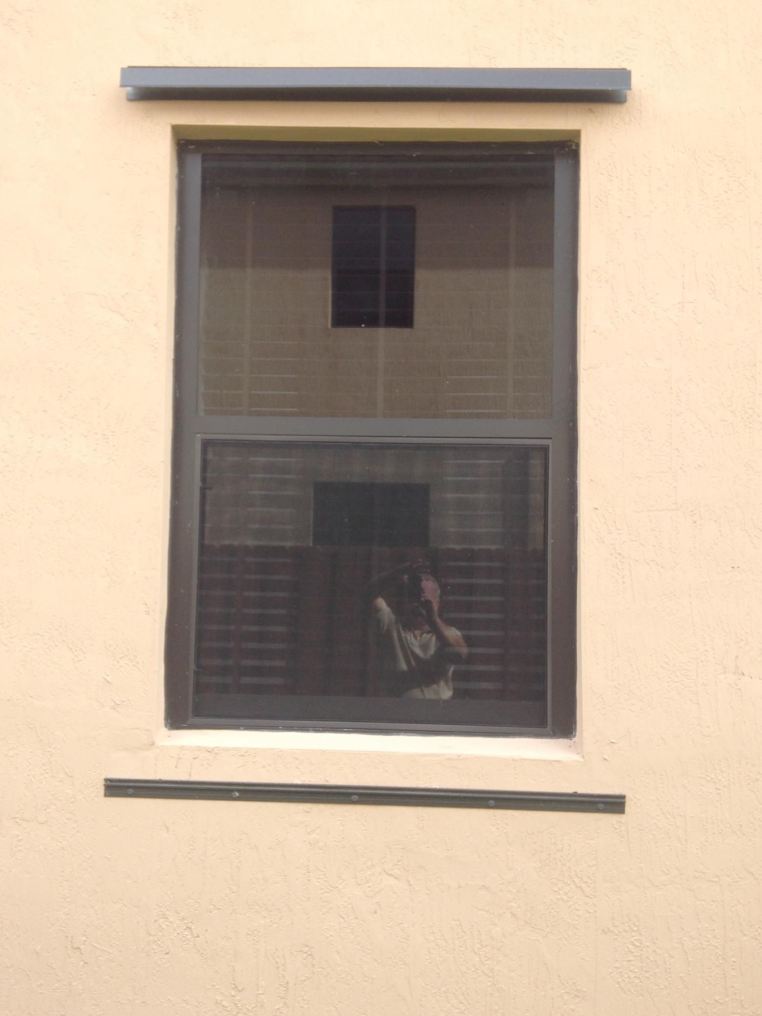 A window on the side of a building with a reflection of a person in it.