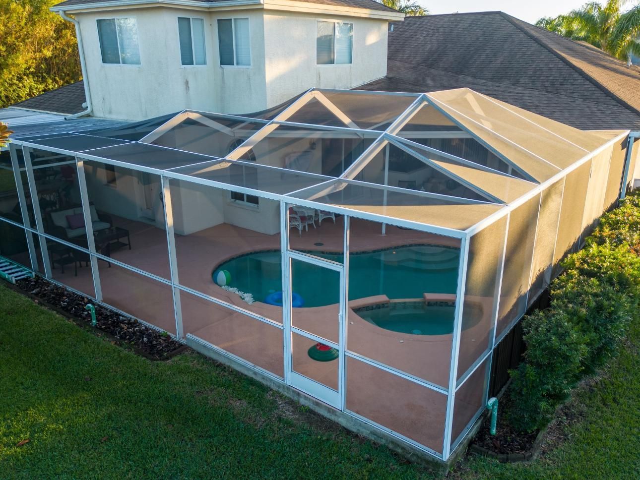 An aerial view of a screened in pool area in front of a house.