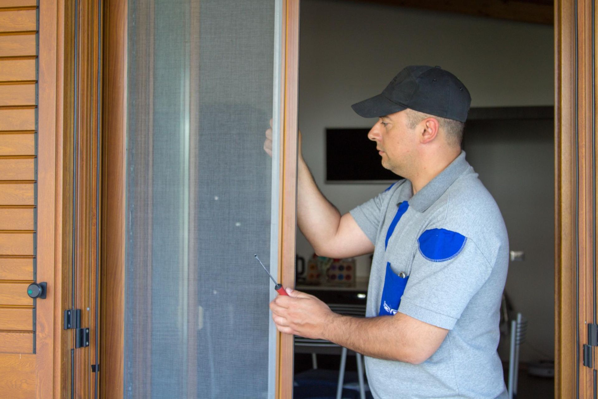 A man is fixing a screen door with a screwdriver.