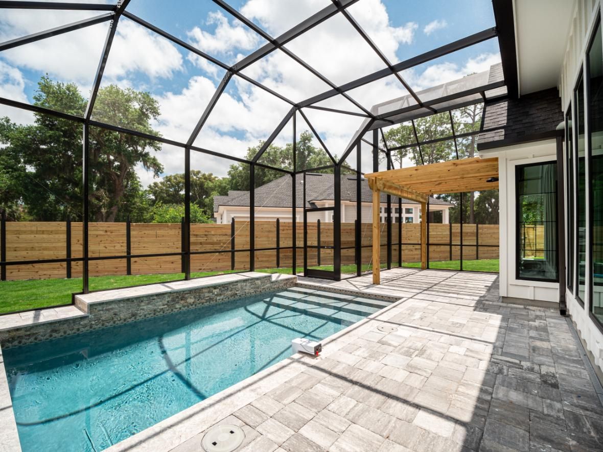 A large swimming pool with a screened in area in the backyard of a house.