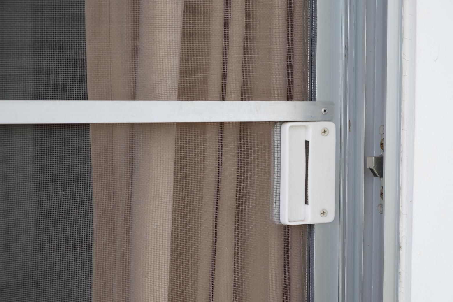 A close up of a screen door with a curtain behind it.