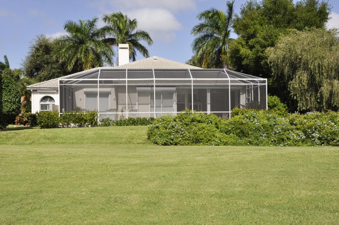 A house with a screened in porch and a large lawn in front of it.