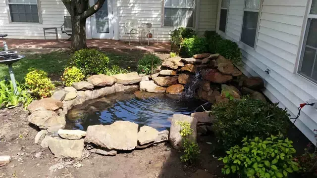 A pond with a waterfall in the backyard of a house.