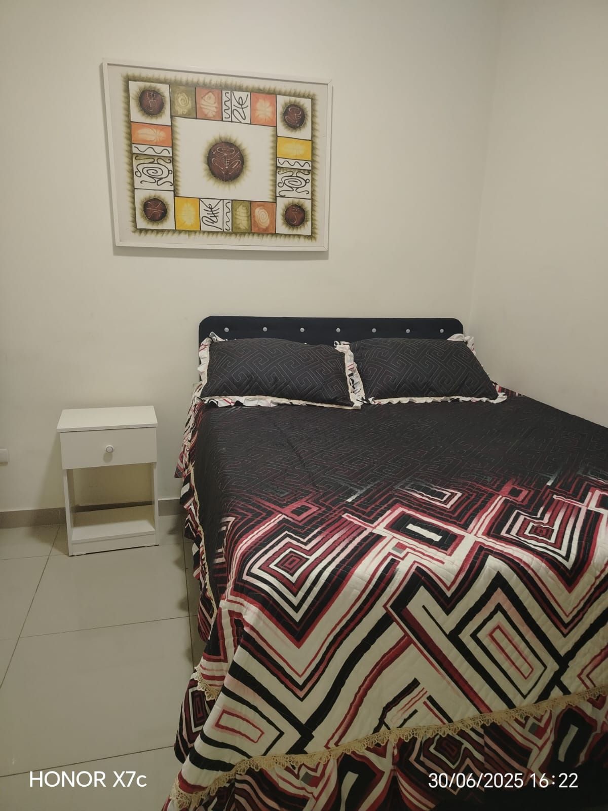 Un dormitorio con una cama, una mesita de noche y un cuadro en la pared.