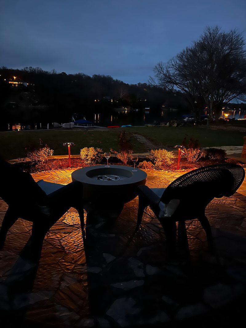 Fire pit with chairs outdoors at dusk. Warm light illuminates the scene, and two glasses sit on the table.