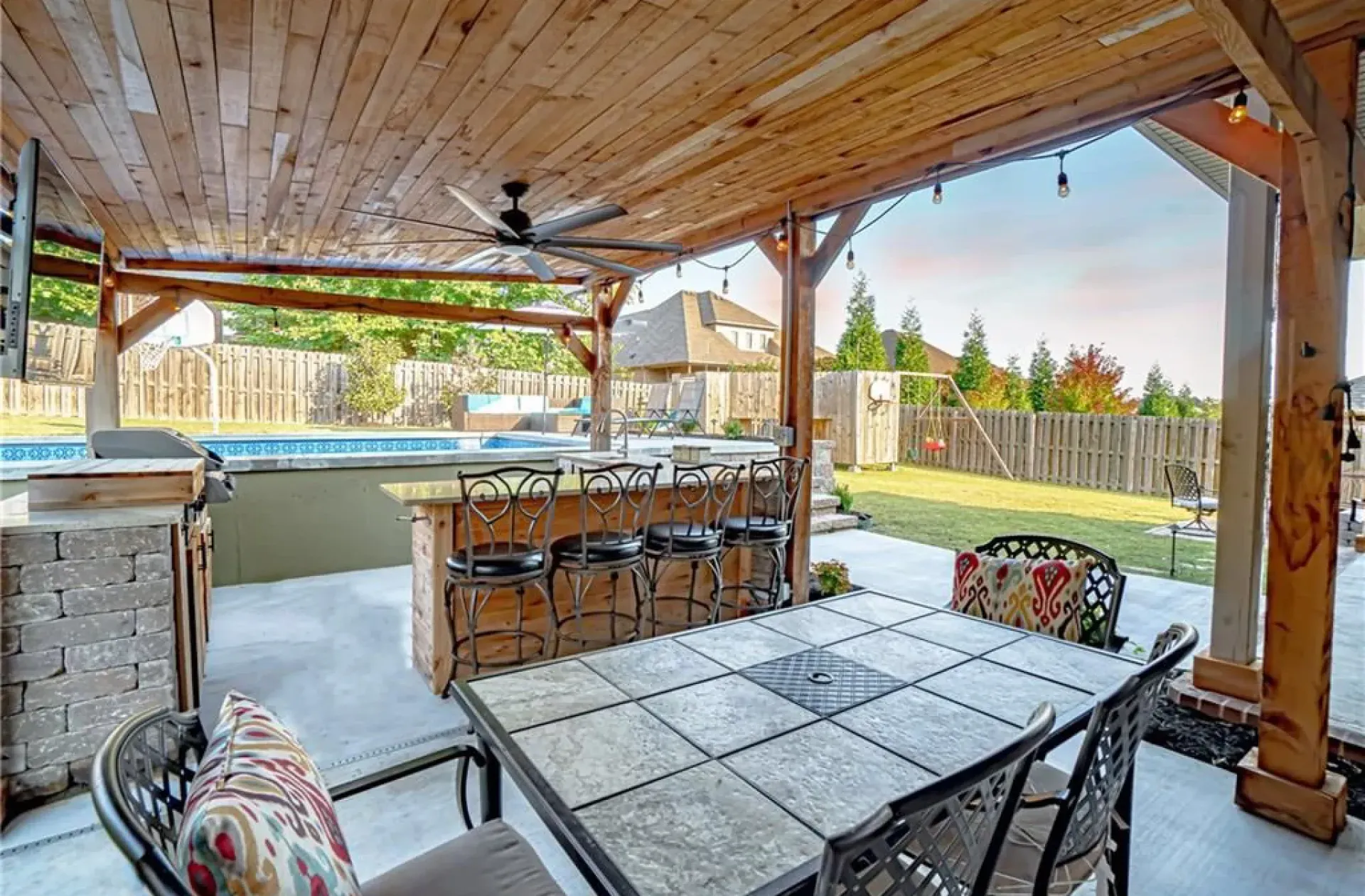 Outdoor patio with a bar, dining table, and swimming pool in the background.