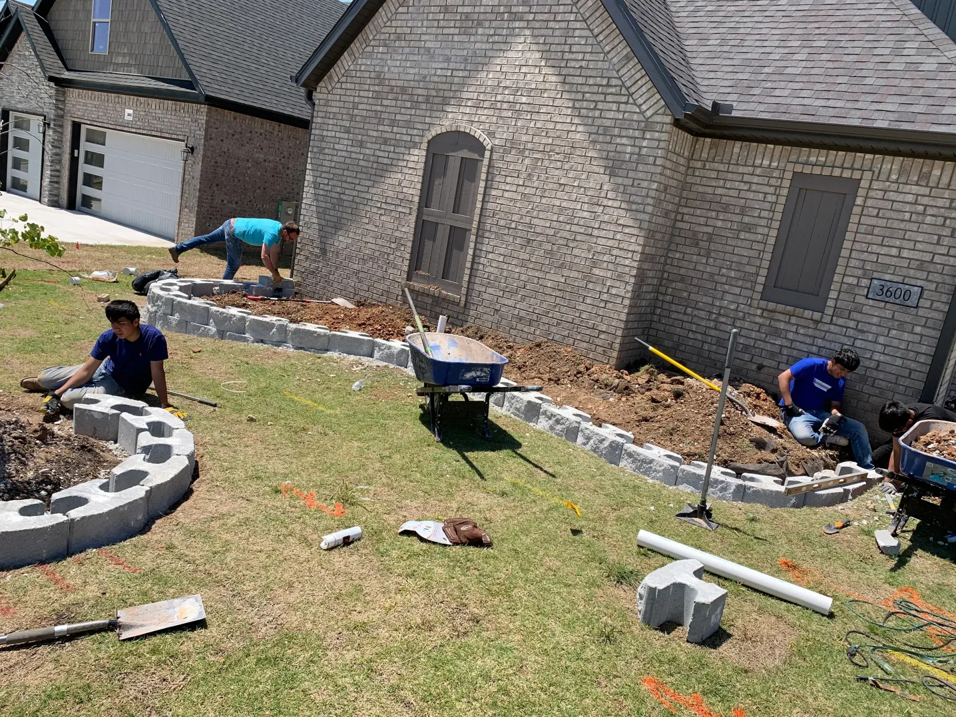 Landscapers building a low stone retaining wall around a brick house.