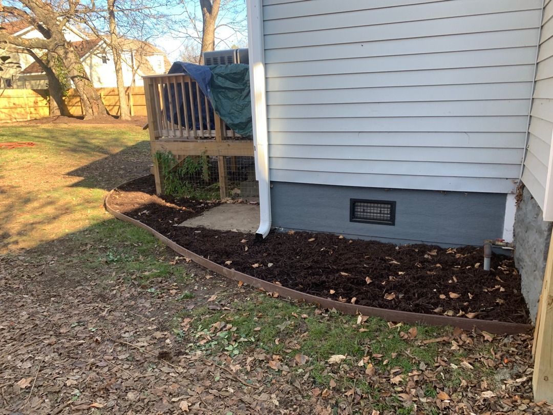 Smiling couple with a child pose outdoors. They wear fall colors: plaid shirts, green sweater, scarf.