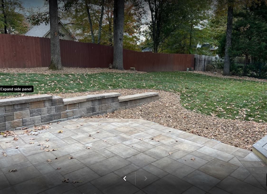 Stone patio with steps leading to a grassy yard with a retaining wall and a wooden fence.