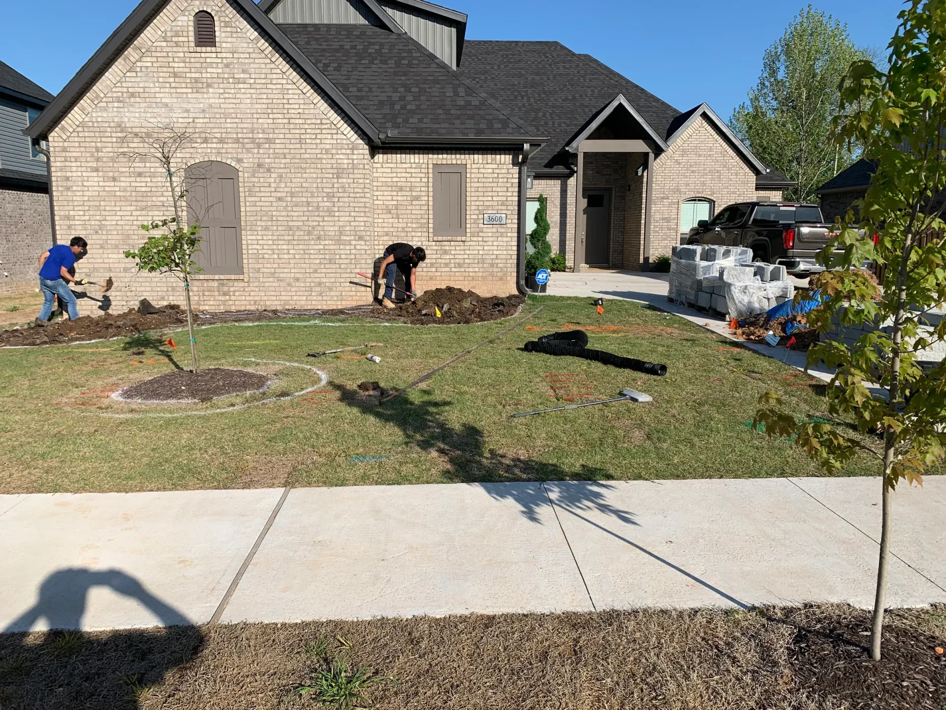 Landscapers working on a front yard with a brick house and new pavers visible.