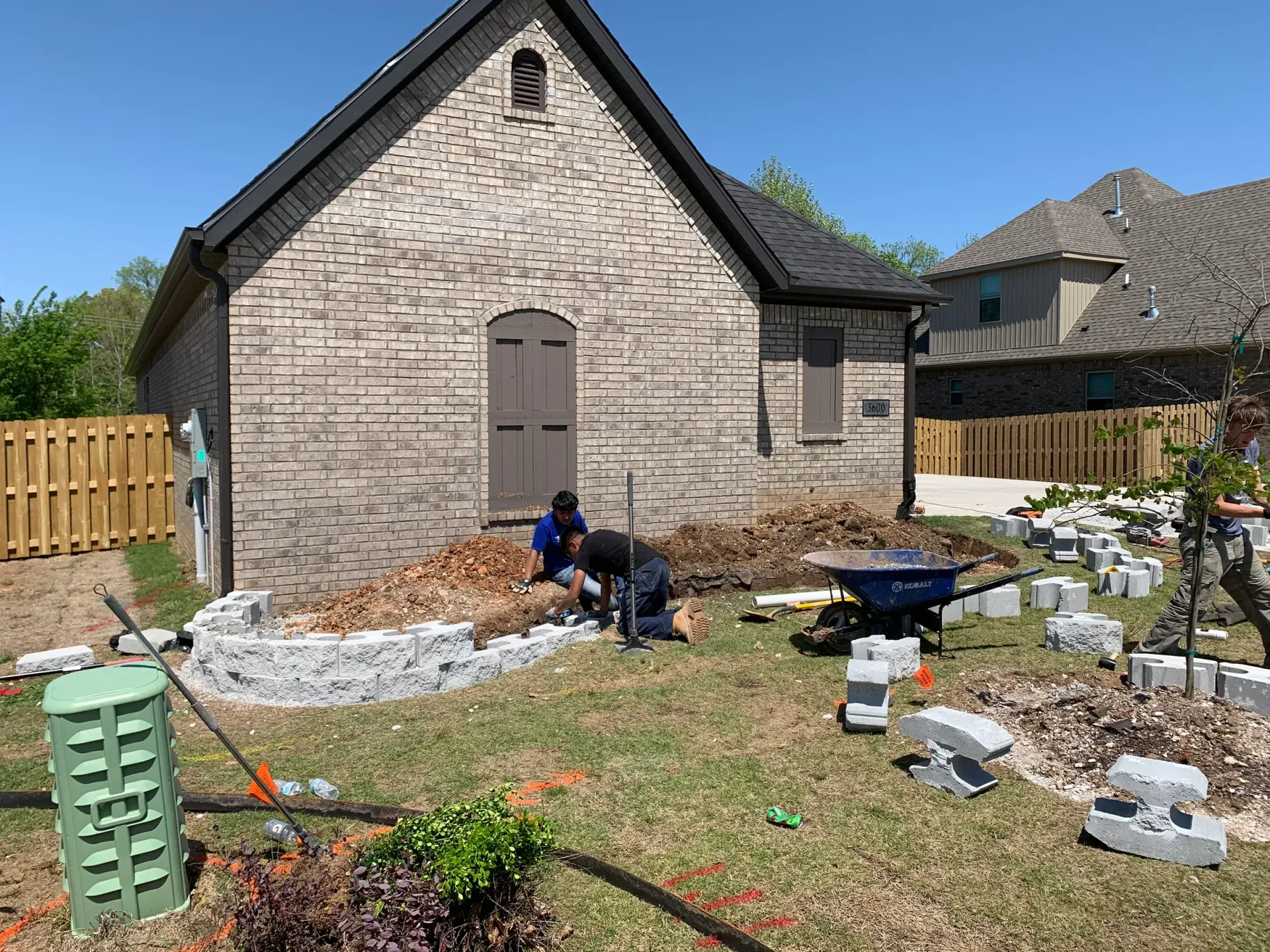 Workers installing landscaping blocks near a brick building.
