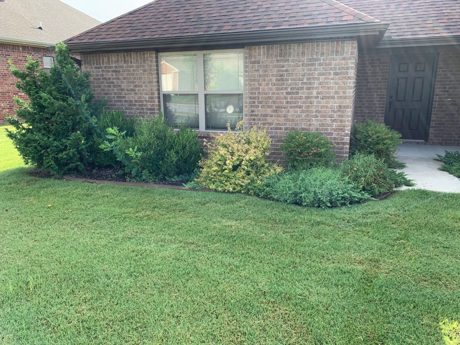 A brick house with a front lawn and bushes. A window and a door are visible.
