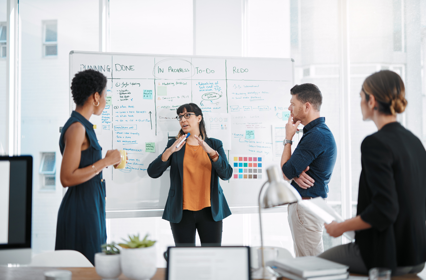A group of people are standing around a whiteboard in an office.